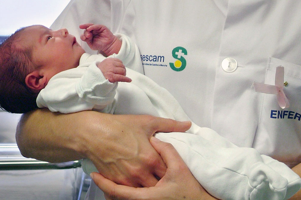 Imagen de archivo en la que una enfermera coge a un recién nacido en brazos. Para ilustrar el gesto de acoger un niño.